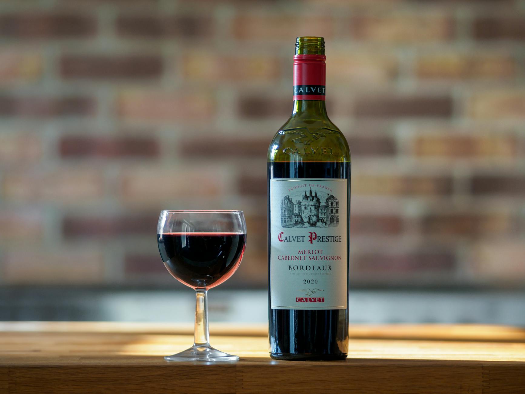 Butelka czerwonego Bordeaux Calvet Prestige i kieliszek na drewnianym blacie