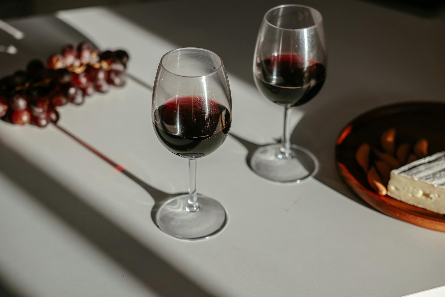 Dwa kieliszki czerwonego Bordeaux z serem brie i winogronami na stole