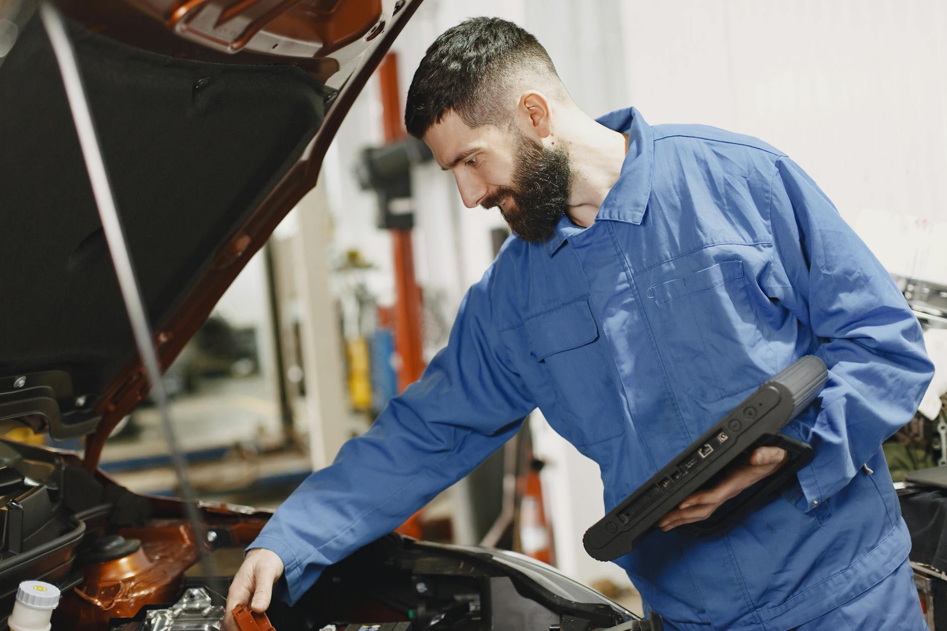 Mechanik w niebieskim kombinezonie sprawdza silnik auta w garażu