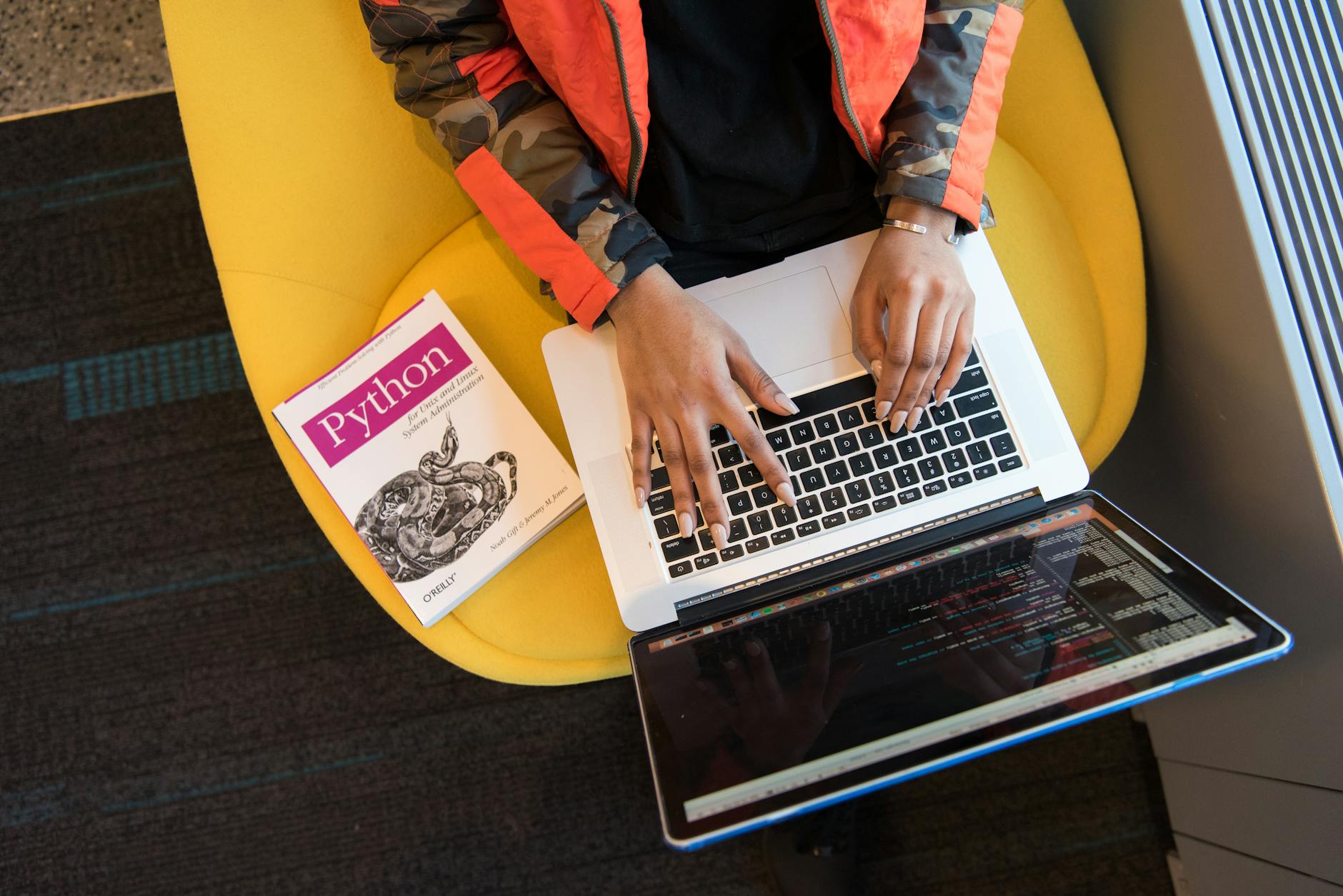 Programista pisze kod na laptopie w biurze obok książki o Pythonie