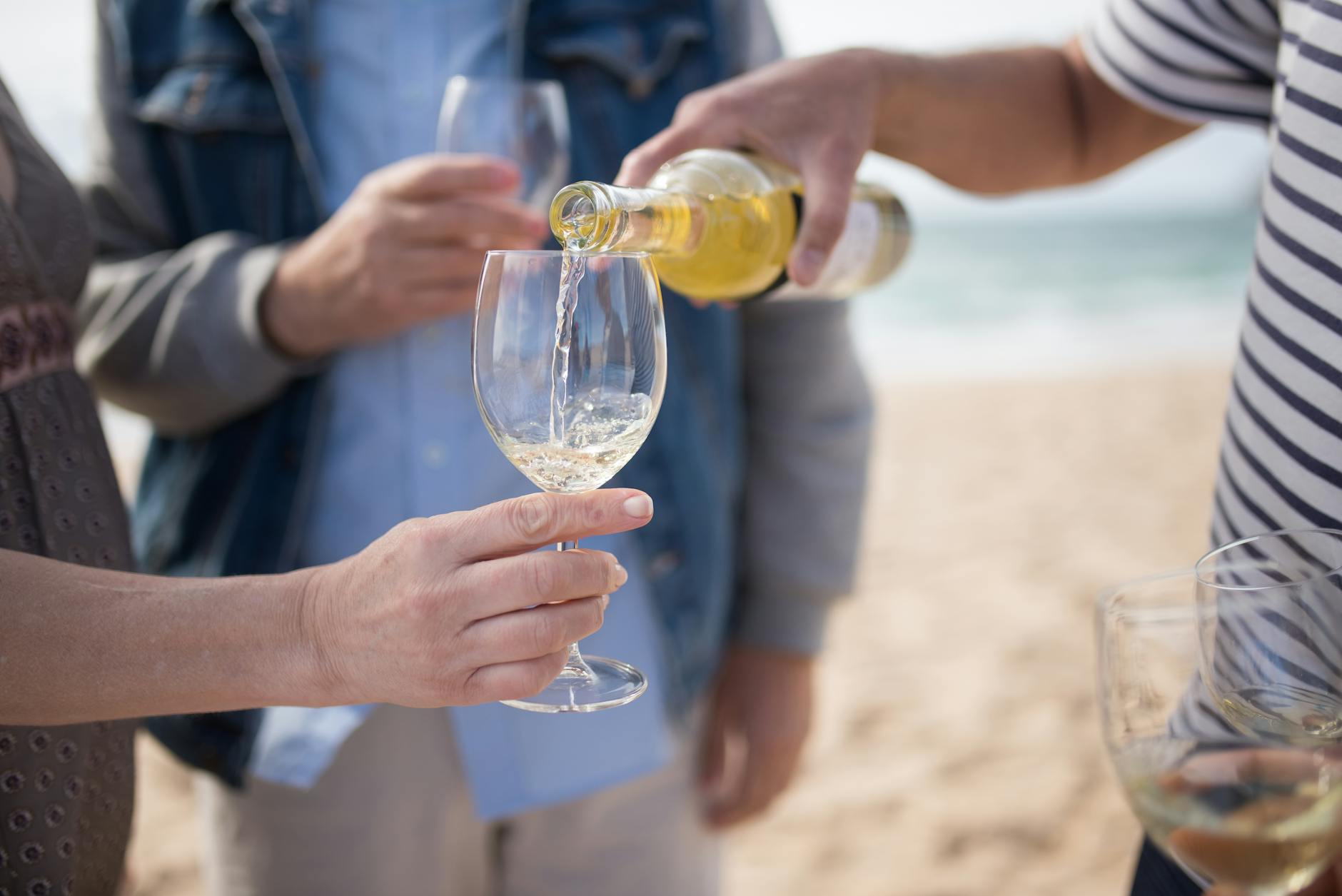 Białe wino nalewane do kieliszków podczas spotkania na plaży Białe wino nalewane do kieliszków podczas spotkania na plaży