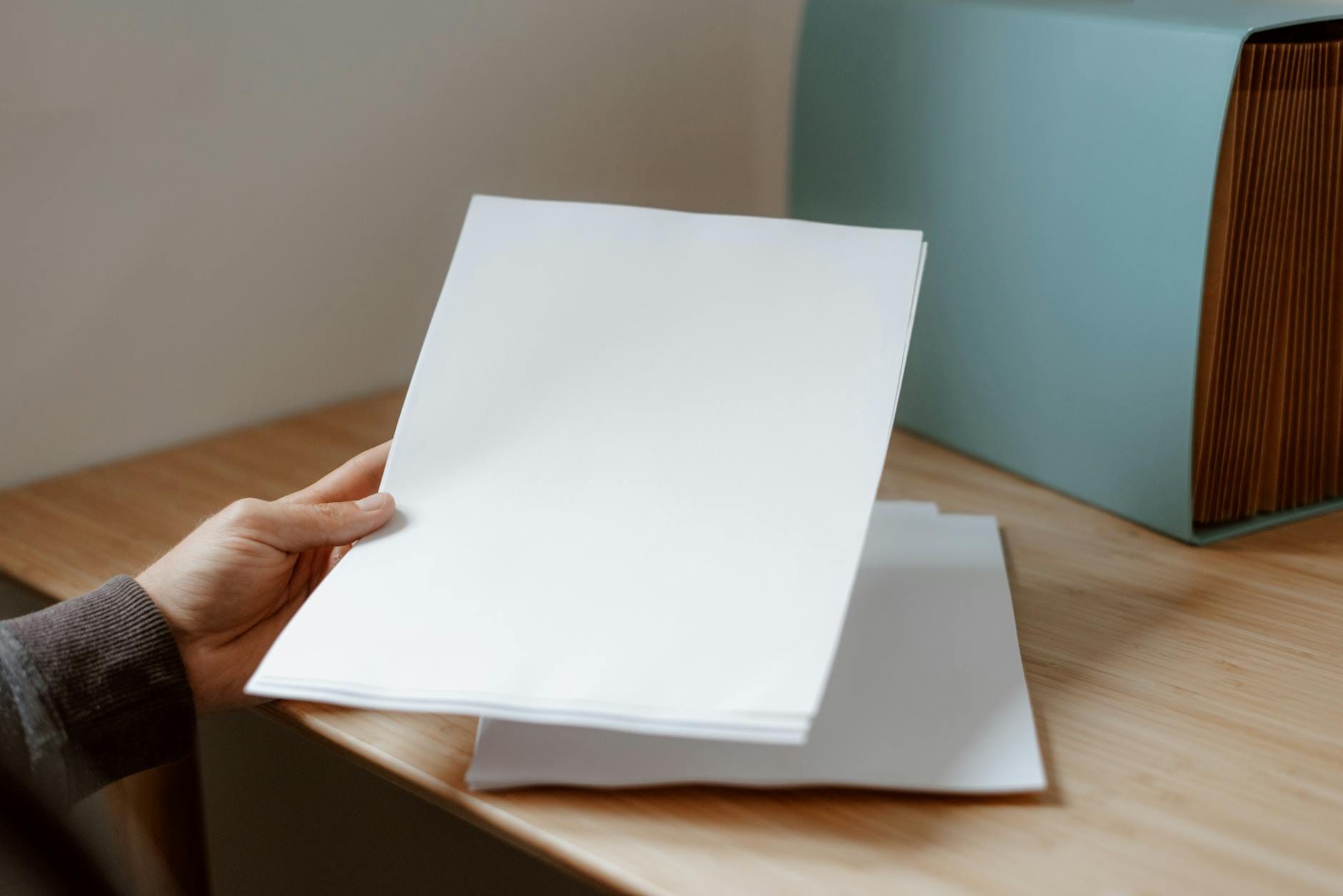 Osoba trzymająca pustą kartkę papieru nad drewnianym biurkiem Osoba trzymająca pustą kartkę papieru nad drewnianym biurkiem