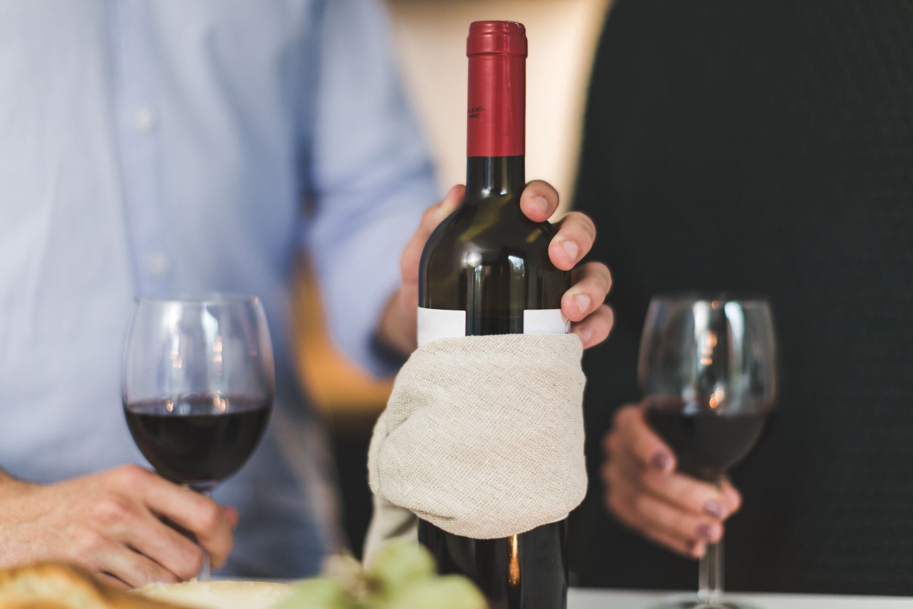 Dwie osoby pijące czerwone wino przy stole z butelką owiniętą tkaniną